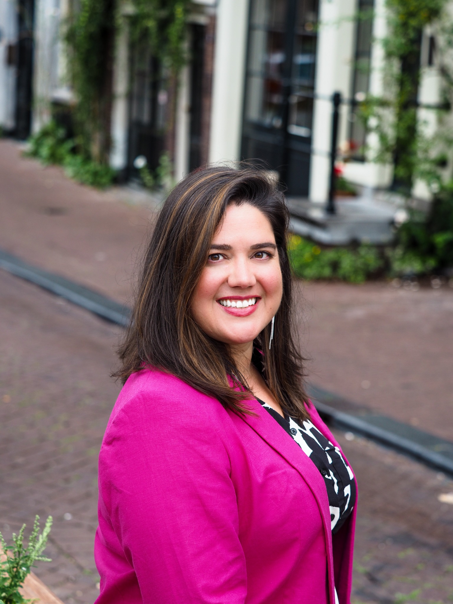 Laurie smiling in a vivid pink jacket on an Amsterdam street